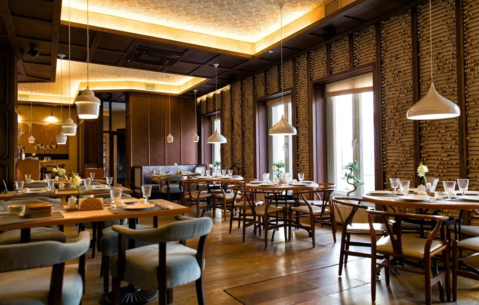 Lichte restaurantzaal met houten tafels, hanglampen en gedekte tafels